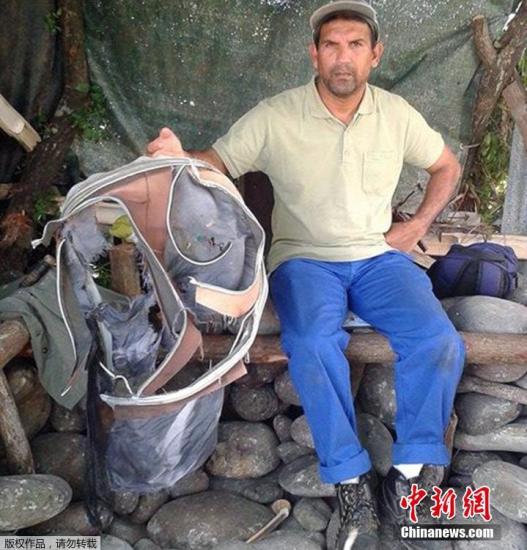 圖為當(dāng)?shù)貢r間7月30日，留尼旺島上的一名海岸清潔人員展示他找到的一個手提箱的殘骸。